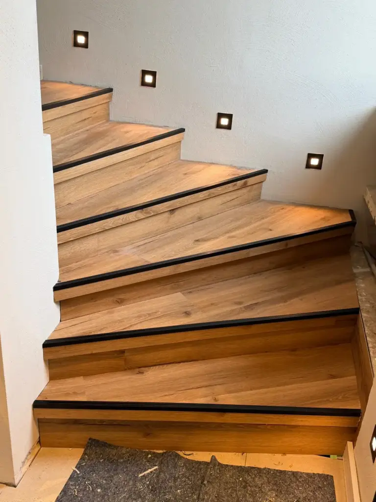 Eine neu verlegte Holztreppe mit schwarzem Trittschutz, umgesetzt von RoGi-Bau.