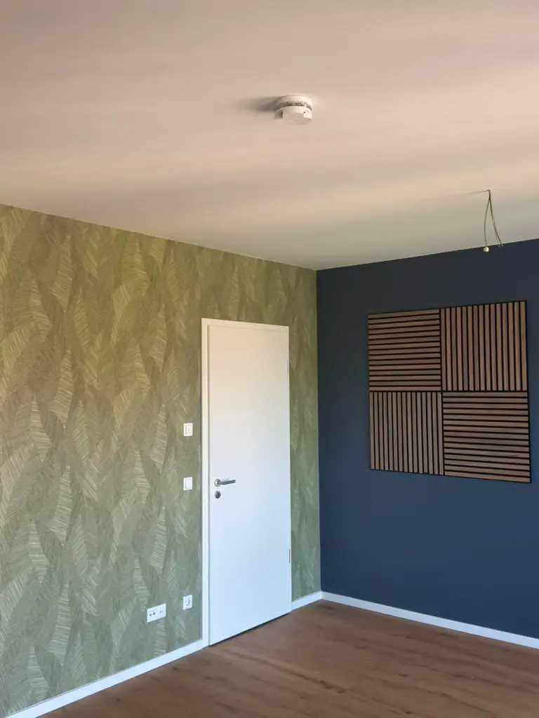Ein Zimmer mit grüner Mustertapete und dunkelblauer Wand mit Akustikpanels, umgesetzt von RoGi-Bau.