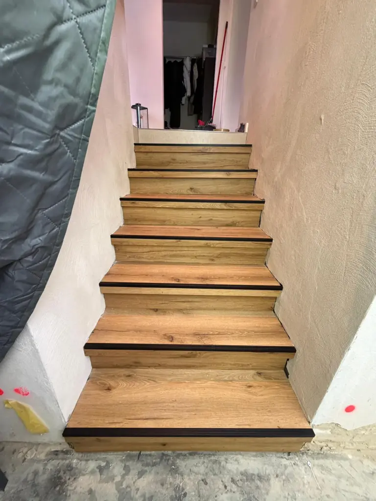 Eine neu verlegte Holztreppe mit schwarzem Trittschutz, umgesetzt von RoGi-Bau.