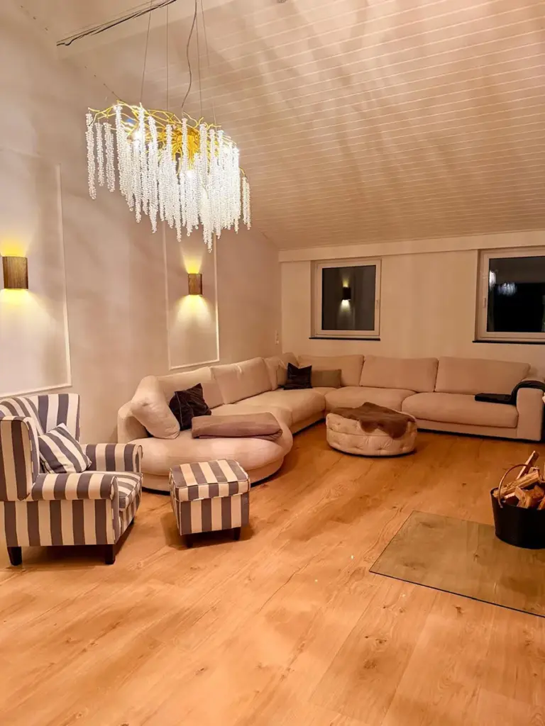 Ein frisch von RoGi-Bau renoviertes, helles weißes Wohnzimmer mit Holzboden und Kronleuchter.