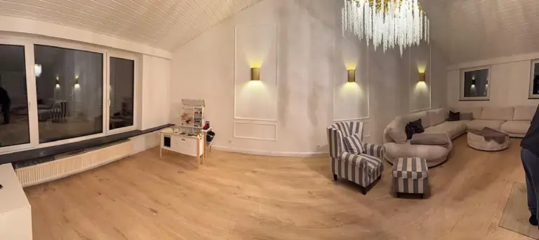 Ein frisch von RoGi-Bau renoviertes, helles weißes Wohnzimmer mit Holzboden und Kronleuchter.