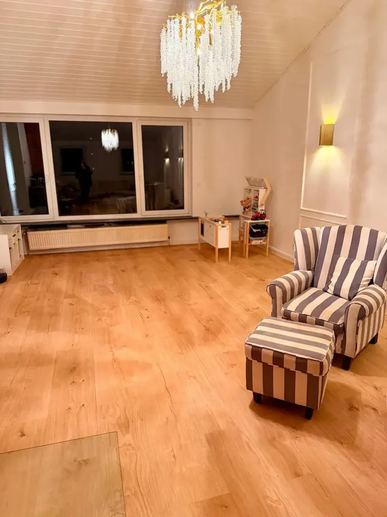 Ein frisch von RoGi-Bau renoviertes, helles weißes Wohnzimmer mit Holzboden und Kronleuchter.