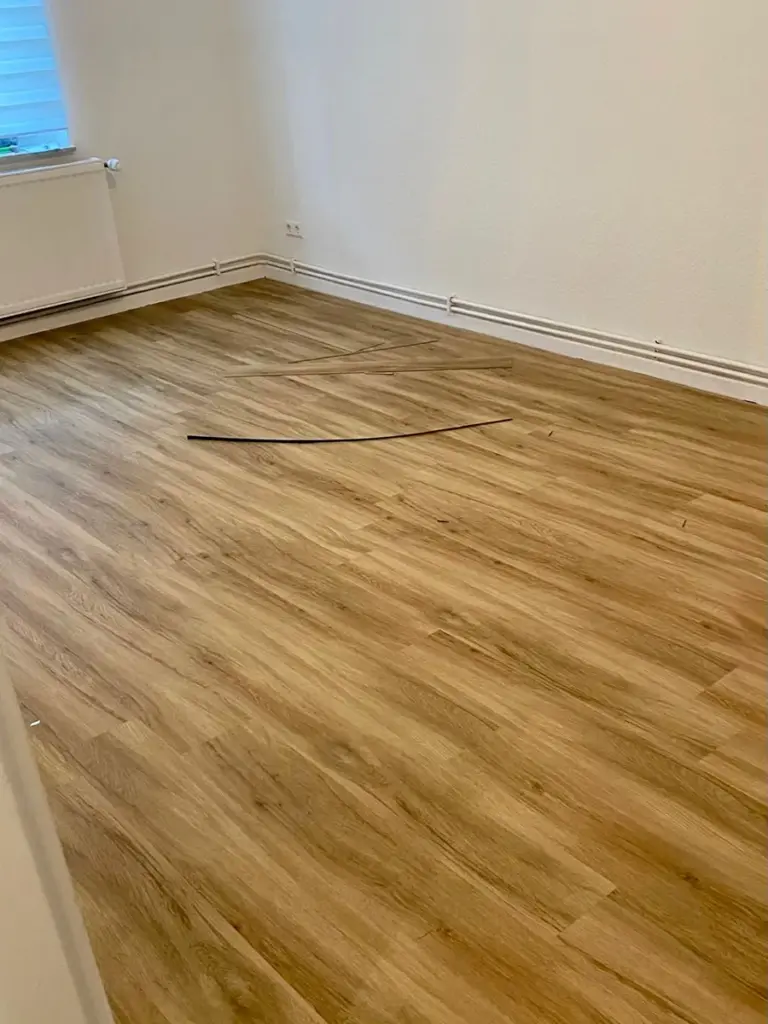 Ein frisch verlegter Laminatboden in einem Raum mit weißen Wänden, umgesetzt von RoGi-Bau.